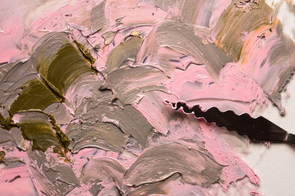 Close-up of textured oil paint strokes in pink and gray with palette knife.